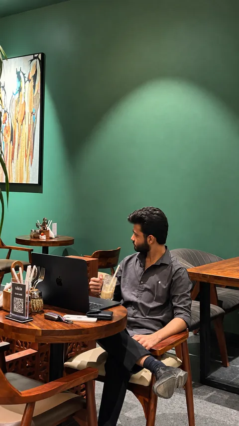 Meet Ranpara working on a laptop at a caf&eacute; table, beside a deep green wall and a framed painting